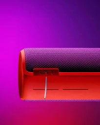 Close-up of a bright red and purple wireless bluetooth speaker against a vivid magenta gradient background