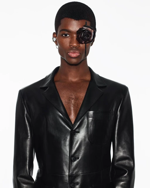 Portrait of a dark-skinned man wearing a black leather jacket and a black rose eye accessory against a white background in a photo studio.