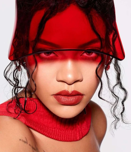 Close-up portrait of a woman with dark curly hair wearing a red visor, red knit top, and red lipstick against a white background.