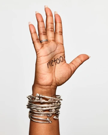 Close-up of a raised hand with handwritten text on the palm, stacked silver bangles, against a neutral white background