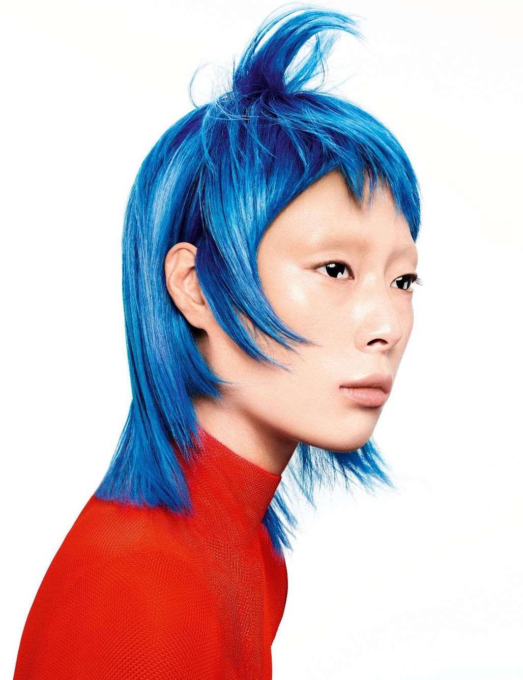 Asian woman portrait with vibrant blue short hairstyle, styled up, wearing a bright red turtleneck sweater against a clean white backdrop.