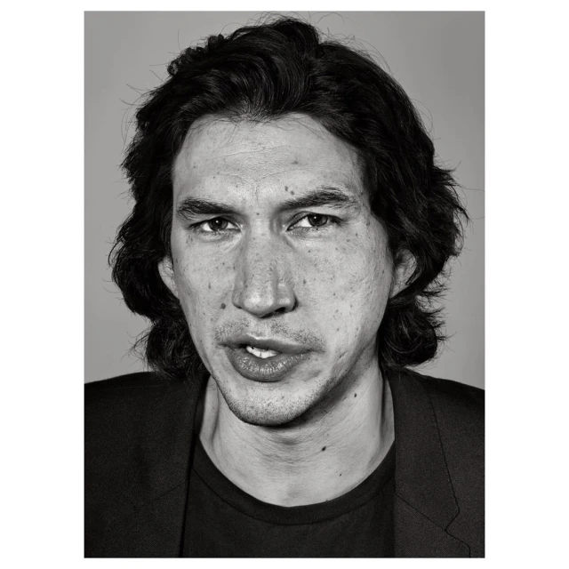 Black and white headshot of actor Adam Driver in a dark jacket against a grey backdrop, capturing a serious yet slightly wry expression.