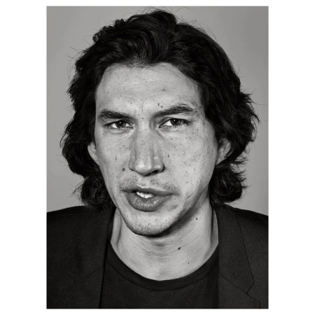 Black and white headshot of actor Adam Driver in a dark jacket against a grey backdrop, capturing a serious yet slightly wry expression.