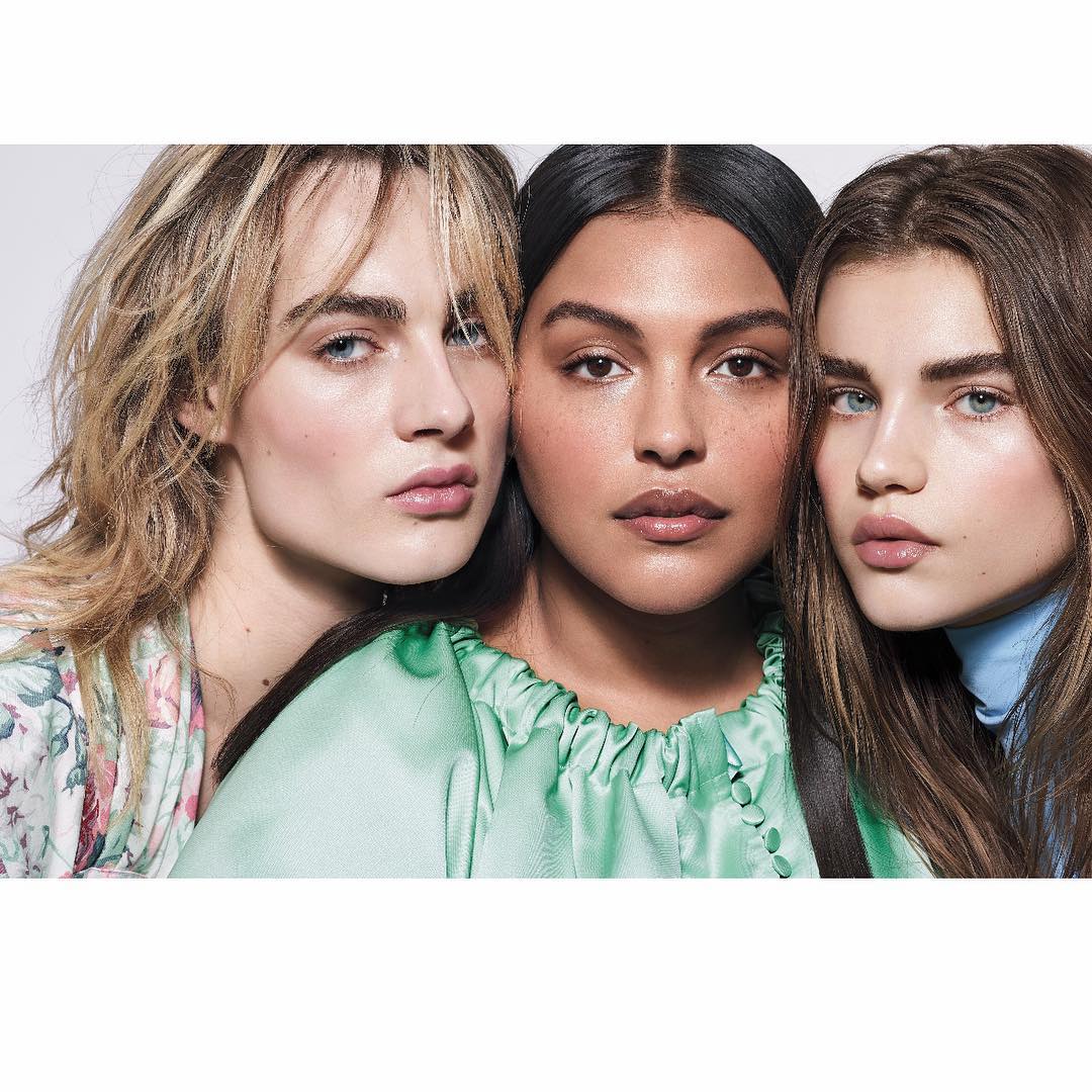 Close-up of three women with light makeup and various hair colors in a photo studio against a neutral background.