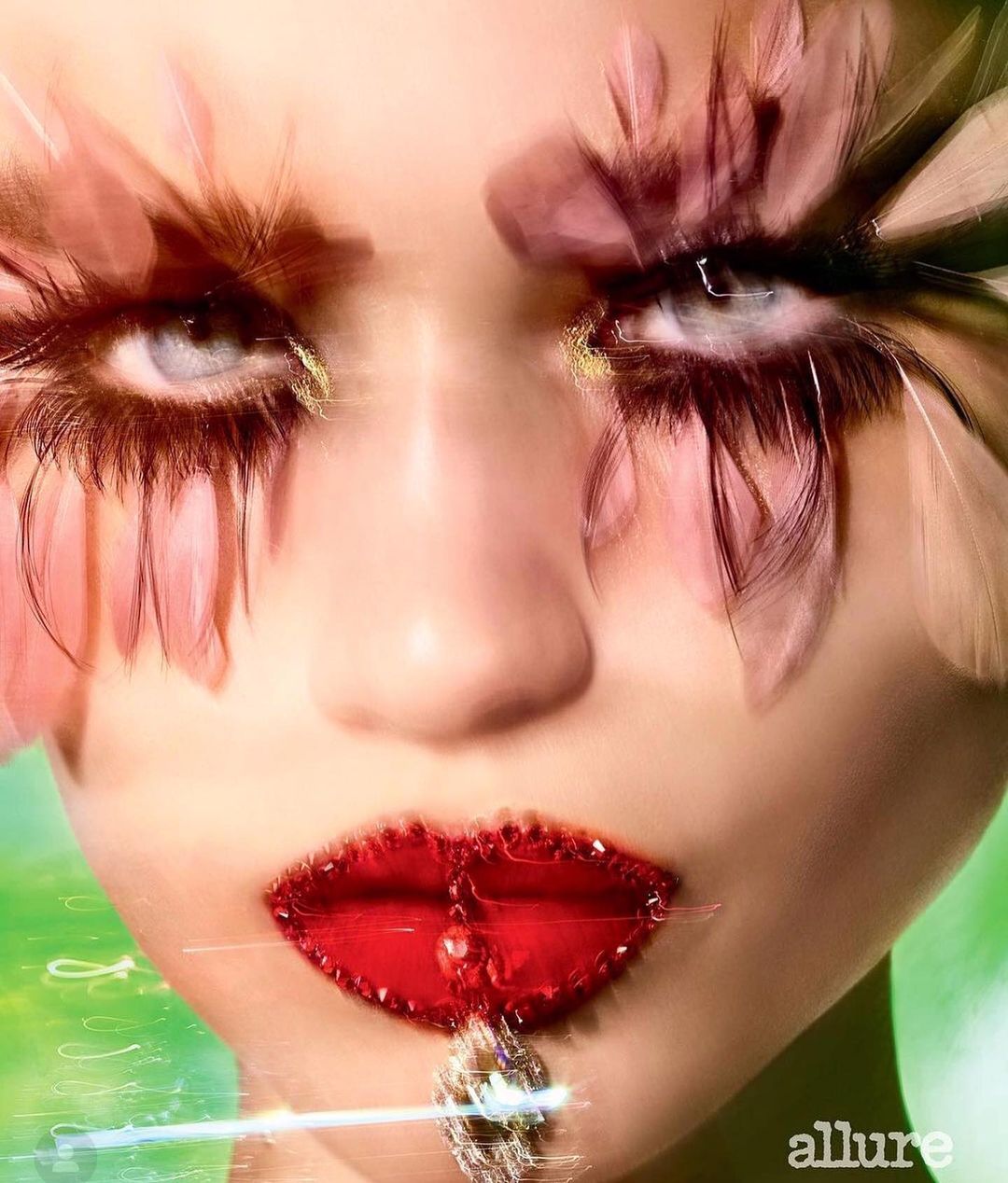 Close-up of an adult female face with red lipstick and dramatic feather eyelashes, set against a blurred green background.