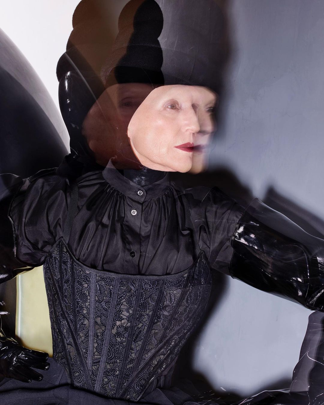 Woman with multiple head images and dark hair in a fashionable black corset top and gloves posing in a photo studio with soft lighting.