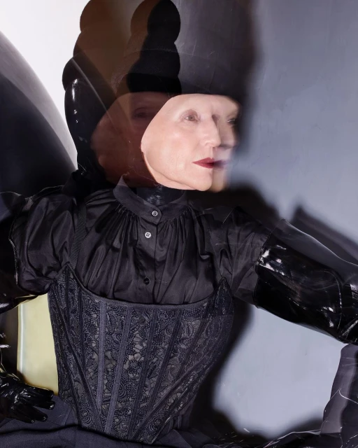 Woman with multiple head images and dark hair in a fashionable black corset top and gloves posing in a photo studio with soft lighting.