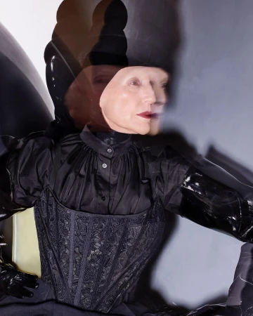 Woman with multiple head images and dark hair in a fashionable black corset top and gloves posing in a photo studio with soft lighting.