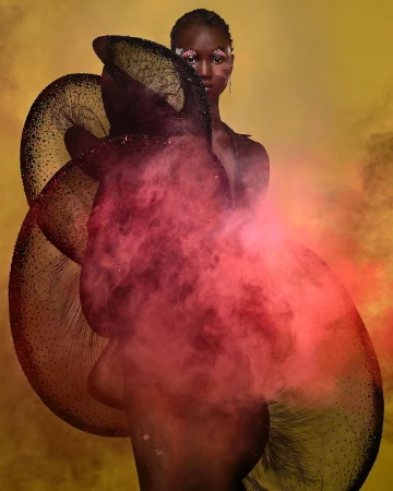 Model wearing a large sculptural dark garment and pink smoke against a warm yellow background