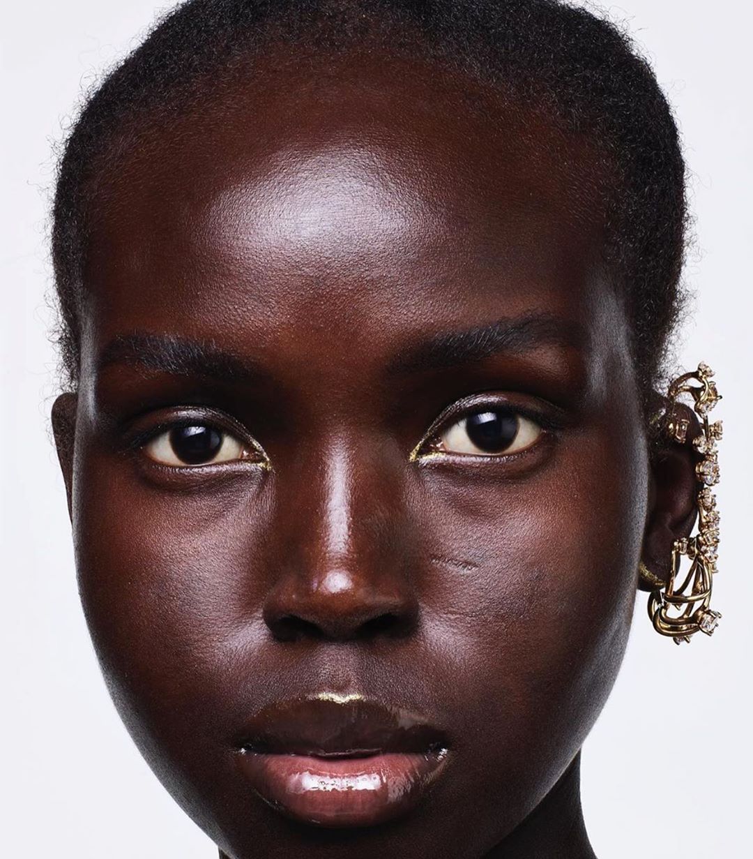 Close-up portrait of a Black woman wearing an elaborate gold ear cuff against a plain white background