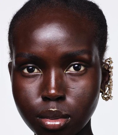 Close-up portrait of a Black woman wearing an elaborate gold ear cuff against a plain white background
