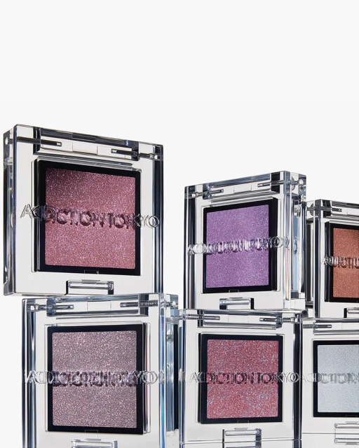 Close-up of stacked ADDICTION TOKYO eye shadow singles in clear cases showcasing pink, purple, and bronze-toned shimmery eyeshadows.
