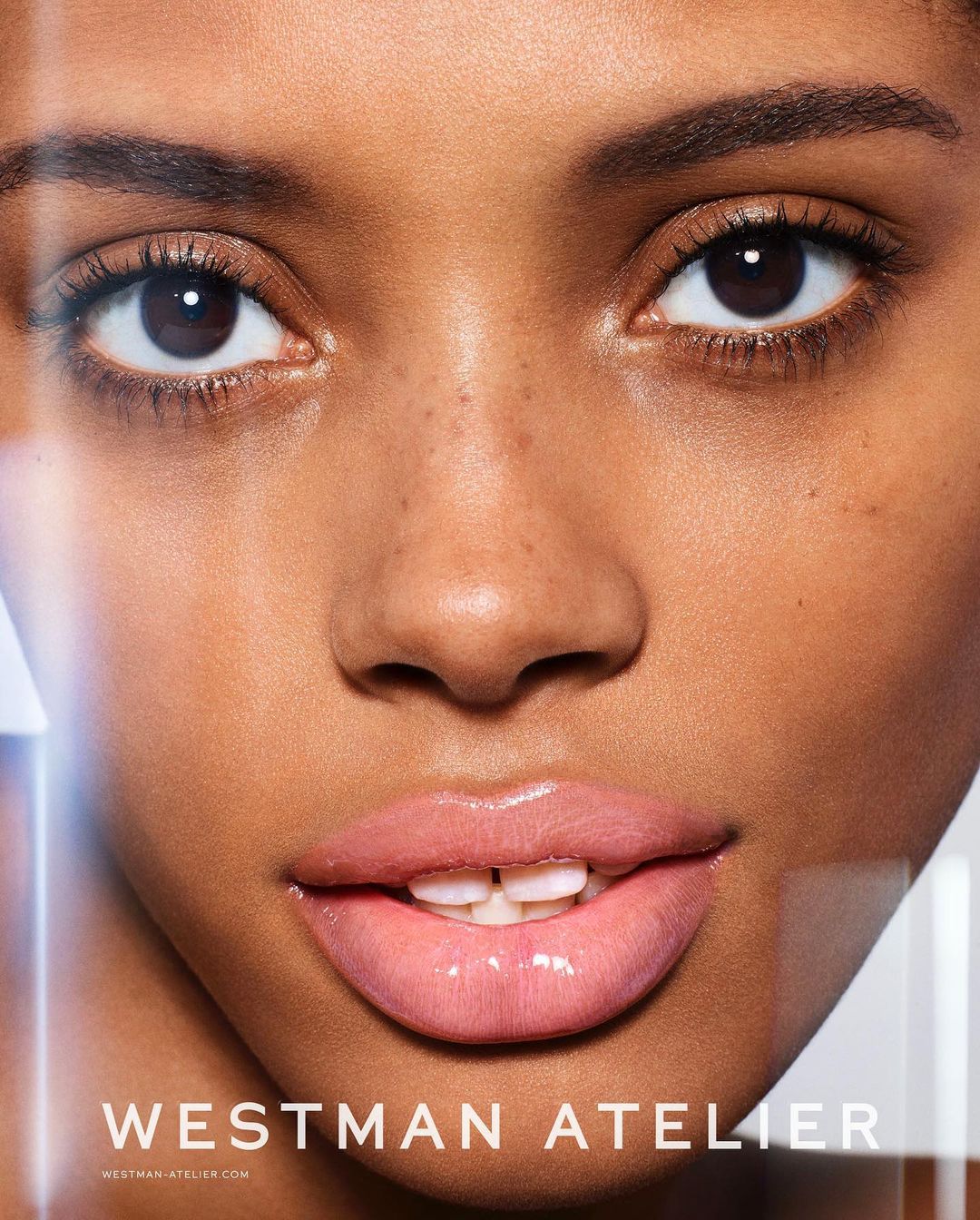Close-up portrait showcasing the face of a Black adult female with brown eyes and pink lips, along with the Westman Atelier logo.