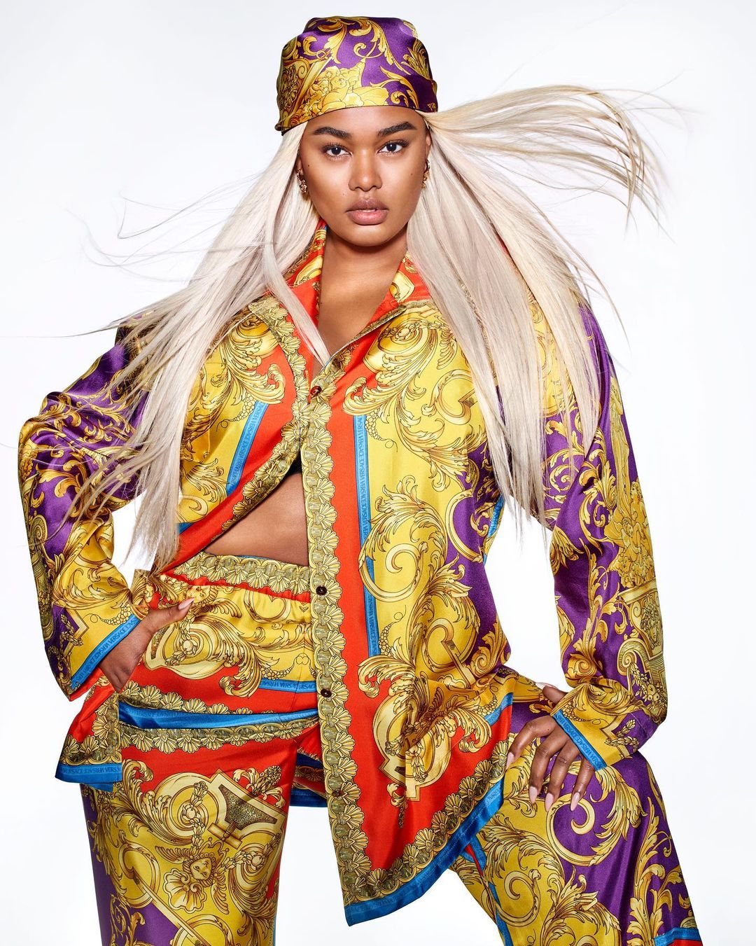 Woman in patterned silk shirt and matching pants and headscarf poses in front of a white backdrop in a beauty and fashion shot.