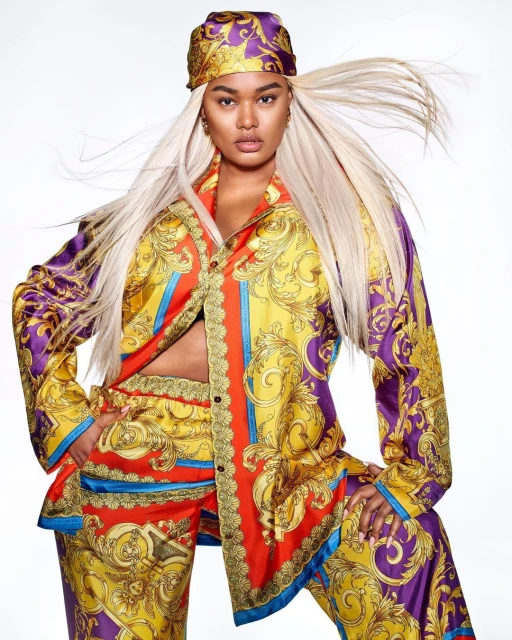 Woman in patterned silk shirt and matching pants and headscarf poses in front of a white backdrop in a beauty and fashion shot.