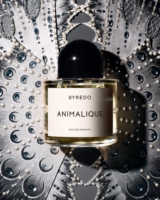 Close-up of Byredo Animalique perfume bottle against a decorative silver and pearl textured background. Beauty and fashion.