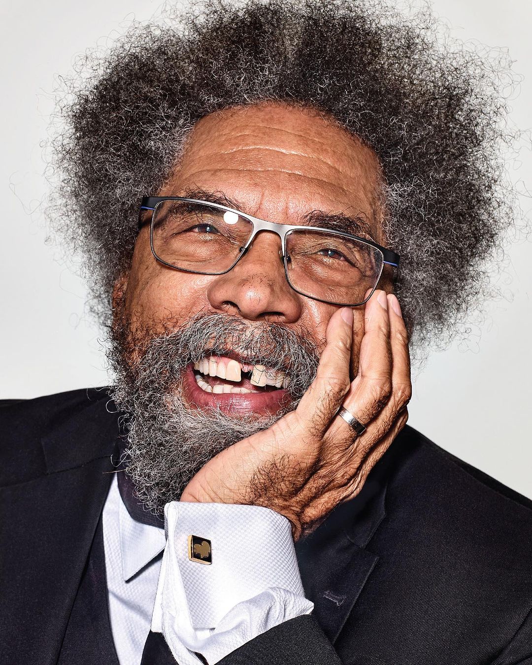 Portrait of an African-American male with glasses and an afro, laughing and resting his face on his hand in a close-up studio shot.