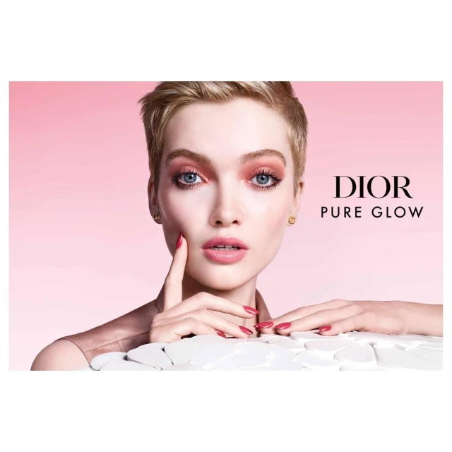 Close-up beauty shot of a blonde female model with pink makeup and matching nail polish in front of a pink background.
