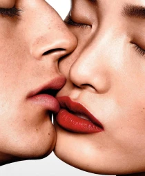 Close-up portrait of two models kissing, featuring vibrant red lipstick against a clean white background by Richard Burbridge.