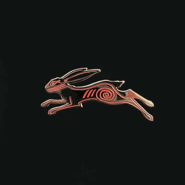 Black and red hare pin. Leaping hare with red spiral design on black background. Metal and enamel accessory for clothing or bags.