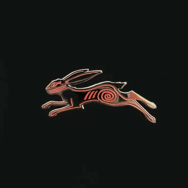 Black and red hare pin. Leaping hare with red spiral design on black background. Metal and enamel accessory for clothing or bags.