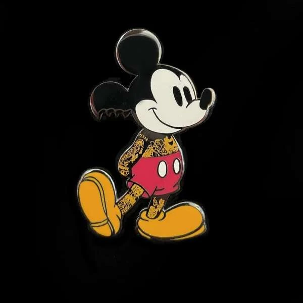 Mickey Mouse pin with tattooed arms and legs, red shorts, and yellow shoes against a black background.