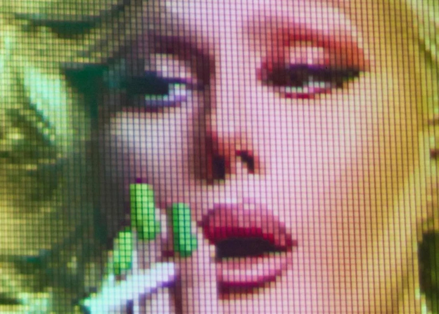 Close-up digital pixelated art of a woman with light skin and blond hair, featuring red lips and manicured green nails.