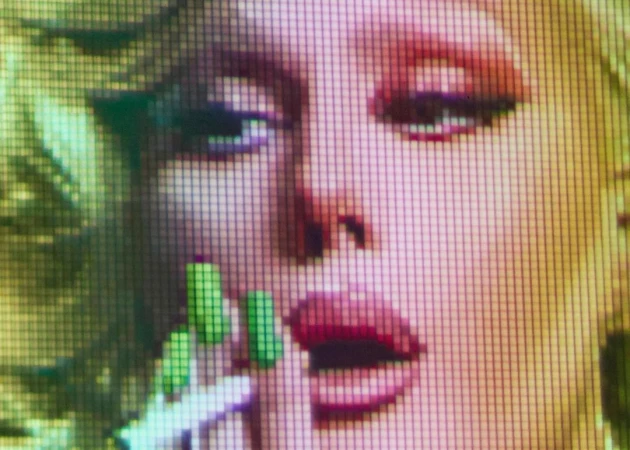 Close-up digital pixelated art of a woman with light skin and blond hair, featuring red lips and manicured green nails.