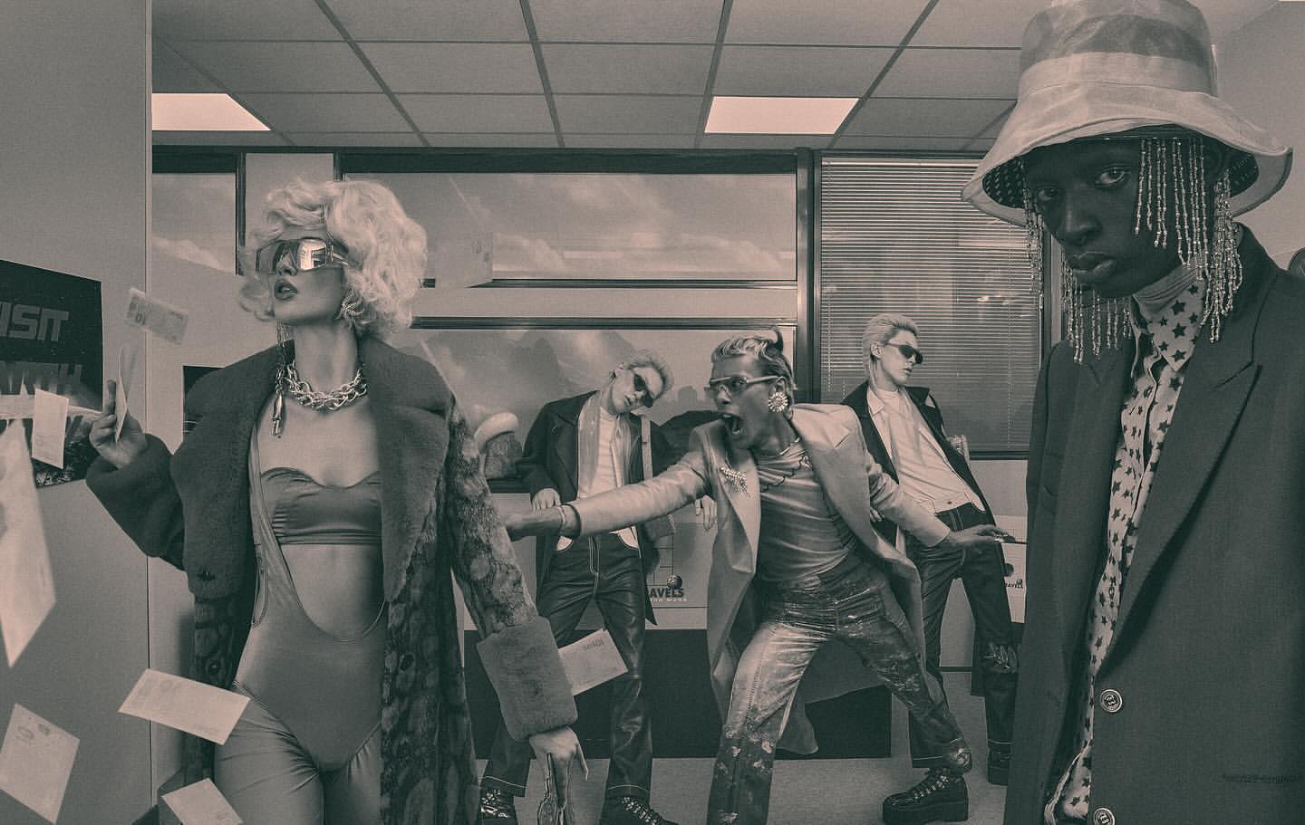 Editorial fashion shot featuring five fashionably dressed adults in an office setting with papers falling, set in monochrome.