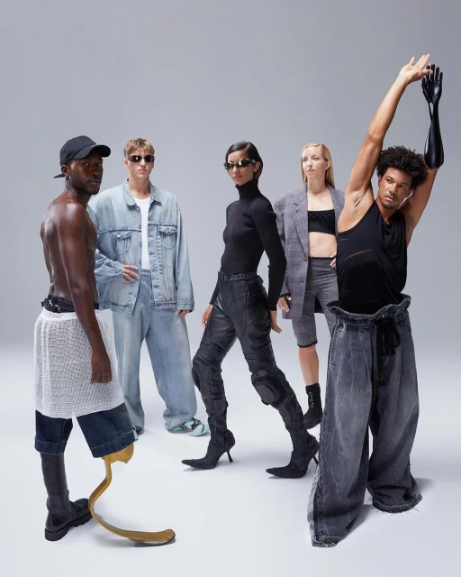 Group of five fashion models in a studio setting, showcasing avant-garde denim and black apparel, some with limb differences, on a neutral background.