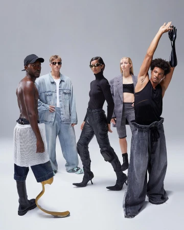 Group of five fashion models in a studio setting, showcasing avant-garde denim and black apparel, some with limb differences, on a neutral background.
