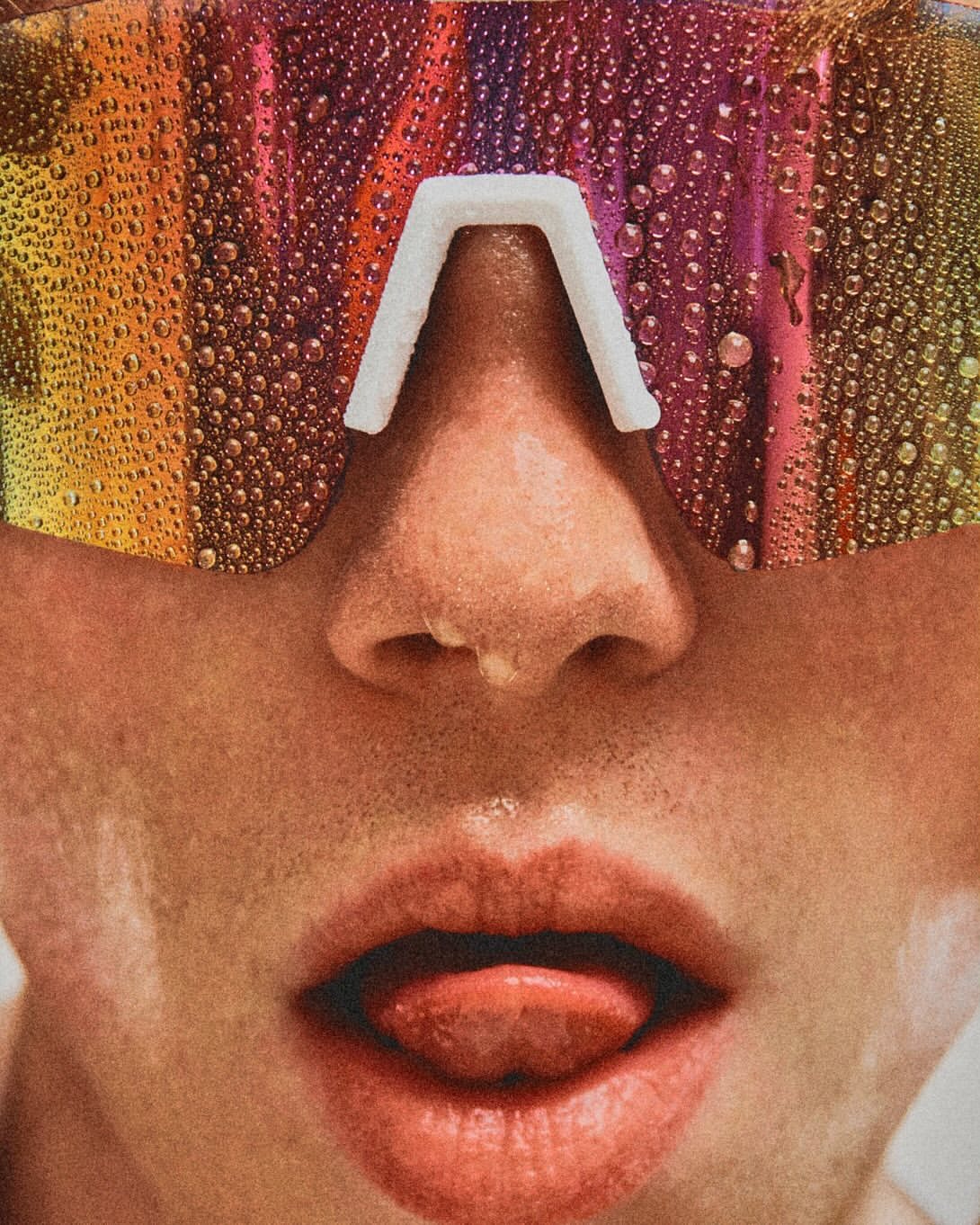 Close-up of a person with iridescent, water-covered visor-style glasses and their tongue sticking out, capturing a surreal, vibrant aesthetic.