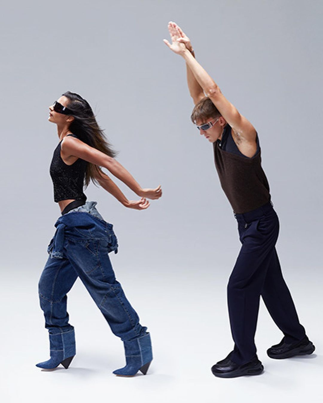 Two fashion models pose indoors in casual, yet stylized clothing, including denim and a vest against a neutral studio background.