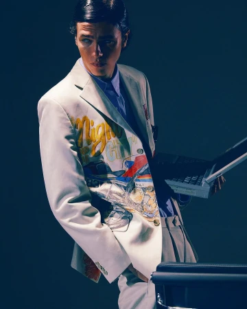 Man wearing a white painted suit jacket holding a laptop in studio lighting photographed by Pictures & Motion