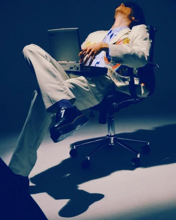 Man in light suit jacket and trousers reclining in an office chair with a laptop, under cool blue studio lighting by Pictures & Motion
