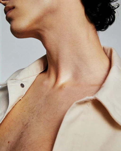 Close-up shot of a fair-skinned young adult with short dark hair, chest and neck visible, wearing a light-colored collared shirt against a white background.