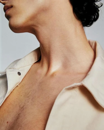 Close-up shot of a fair-skinned young adult with short dark hair, chest and neck visible, wearing a light-colored collared shirt against a white background.