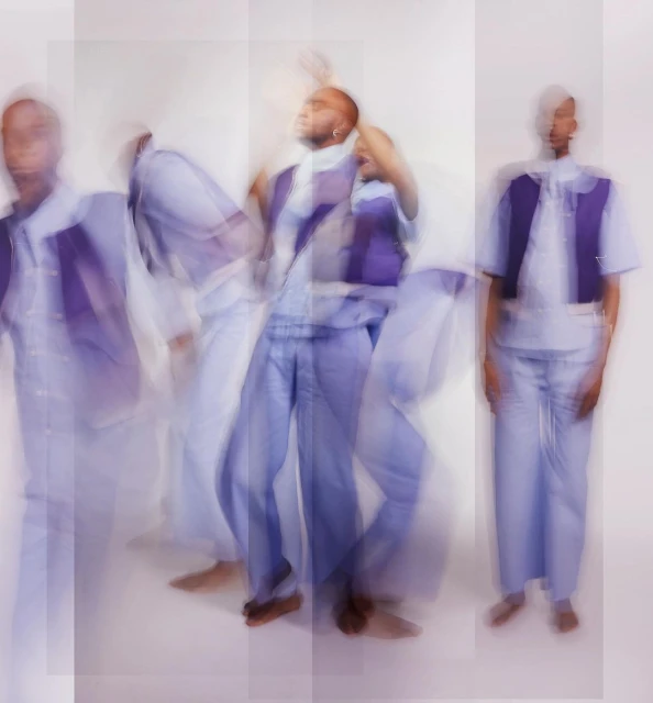Multiple exposures of a black male fashion model in motion, wearing a periwinkle-blue outfit against a white backdrop in a photo studio.