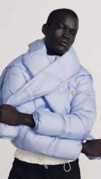 Portrait of a black man wearing a light blue puffer jacket and scarf against a plain background.