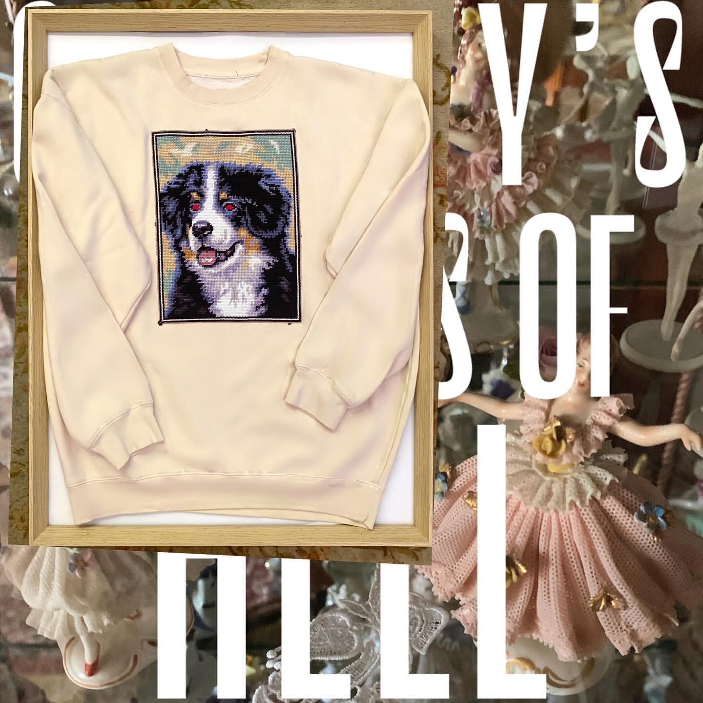 Sweatshirt with a dog portrait on display with vintage dolls in the background. The shirt is framed in a wooden frame.