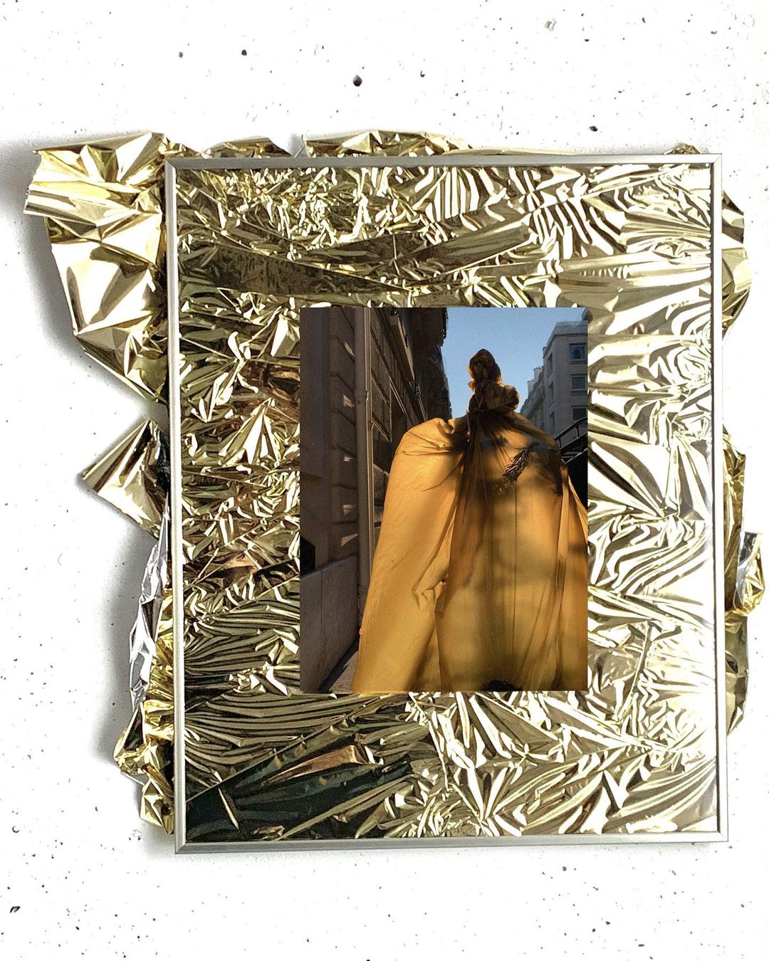 A gold foil frame contains a photographic print of a woman standing in an urban setting, shot from behind, creating a unique, textured artwork.