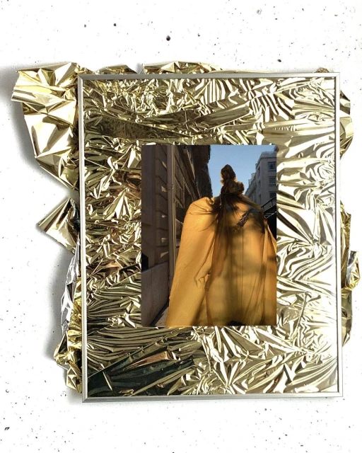 A gold foil frame contains a photographic print of a woman standing in an urban setting, shot from behind, creating a unique, textured artwork.