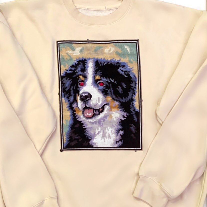 Sweatshirt with a needlepoint of a Bernese Mountain Dog. Dog has black, brown, and white fur and is smiling with an open mouth.