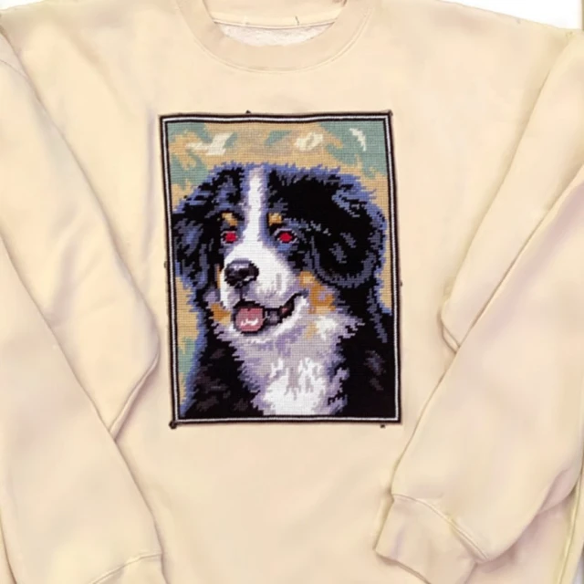 Sweatshirt with a needlepoint of a Bernese Mountain Dog. Dog has black, brown, and white fur and is smiling with an open mouth.