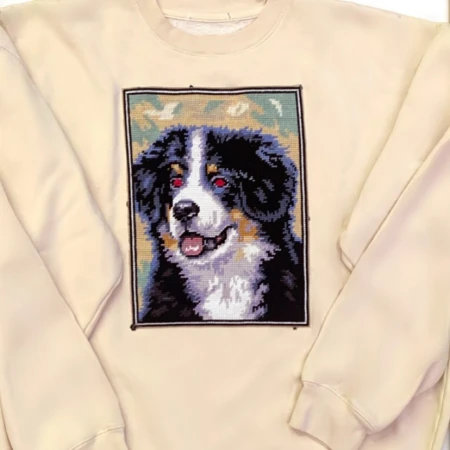 Sweatshirt with a needlepoint of a Bernese Mountain Dog. Dog has black, brown, and white fur and is smiling with an open mouth.