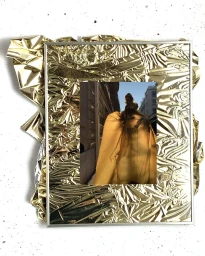 Mixed media illustration featuring a framed photograph of a figure in a gold wrap against a crumpled foil background