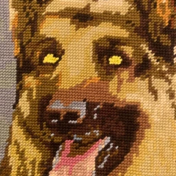 Close-up needlepoint embroidery artwork depicting a dog face with visible textured stitches