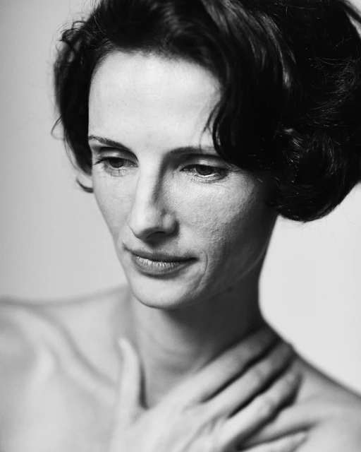 Monochrome portrait of adult woman with dark hair, fair skin, and hand on her neck in a close-up studio shot against a plain background.