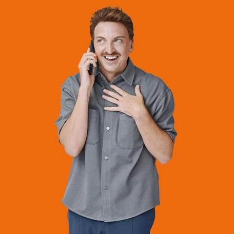 Adult male with a mustache in gray button-down shirt talking on cell phone with an orange background in an indoor photo studio.