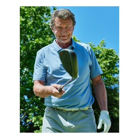 Adult male golfer holding a golf club on the green outdoors. The sky is blue, and trees are visible in the background.